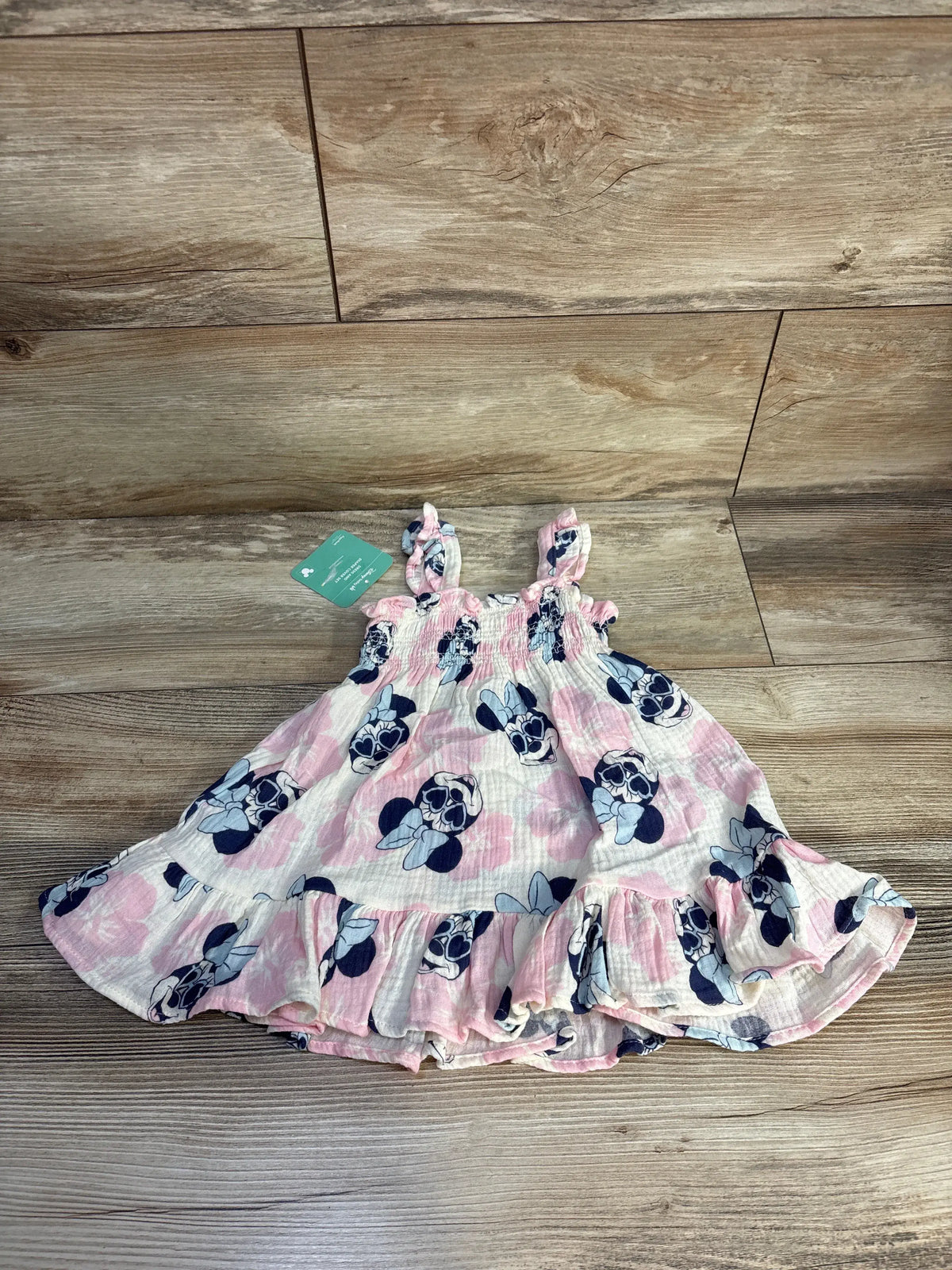 Front view of pink Minnie Mouse smocked gauze dress and bloomers set with smocked bodice and ruffled hem on wood floor