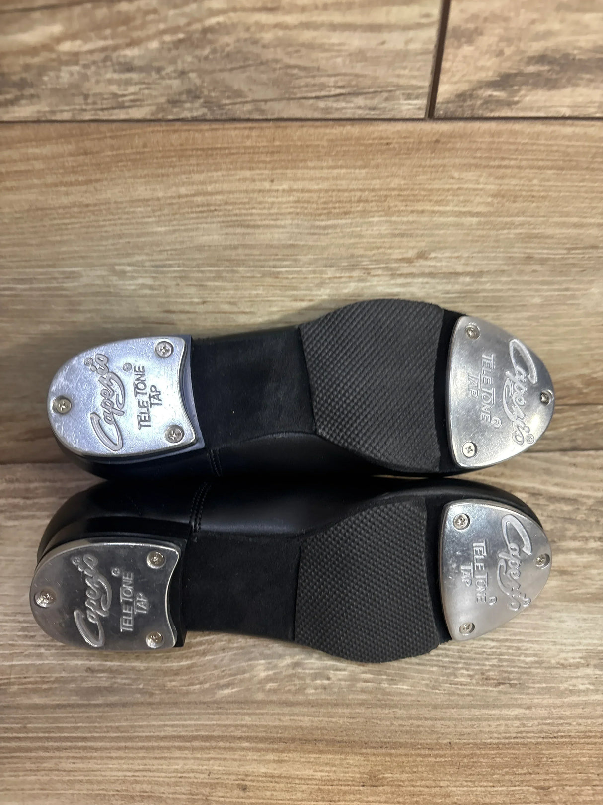 Pair of black Capezio Tele Tone Tap tap shoes with metal taps on wooden floor