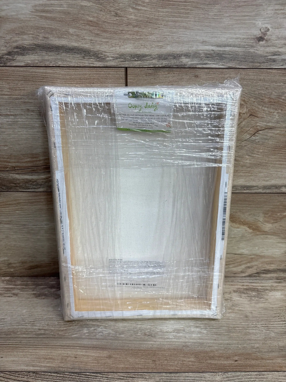 Back view of Oopsy Daisy Cow painting by Stephanie Sliwinsky showcasing its wood frame and clear shrink wrap on a wood floor