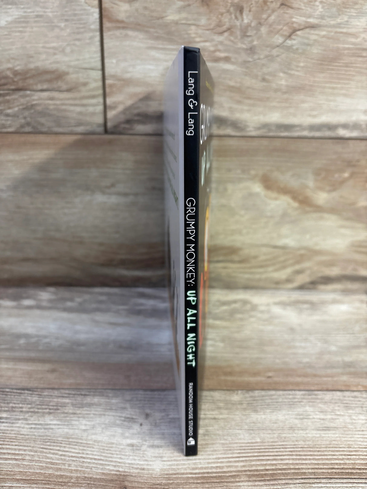 Side view of Grumpy Monkey: Up All Night hardcover showing thin black spine with title visible on wood background