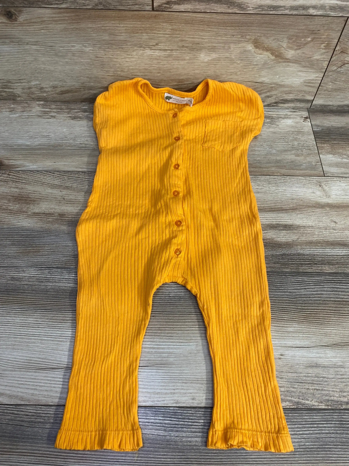 Bright yellow ribbed baby jumpsuit with buttons and small chest pocket on wood floor