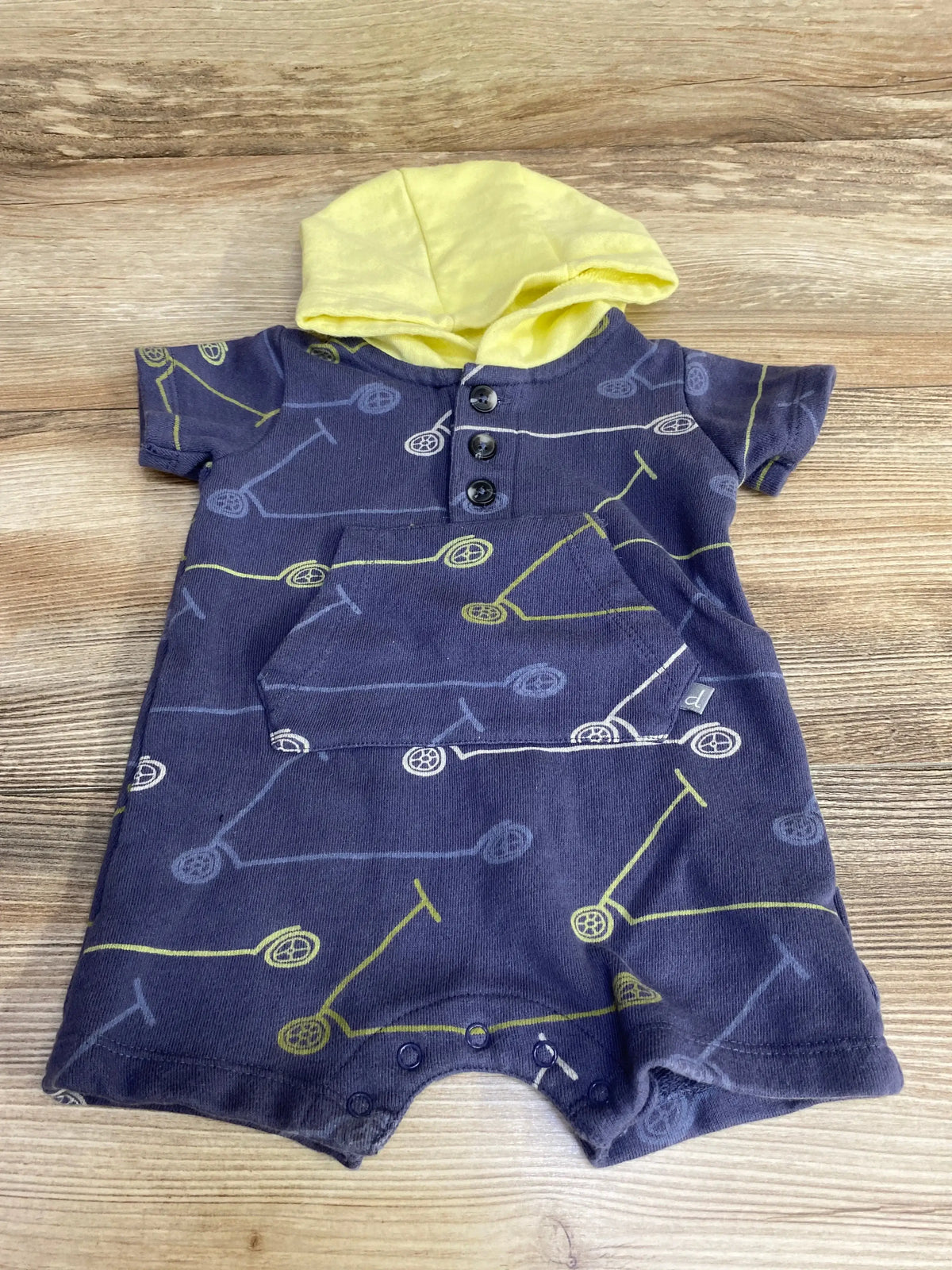 Front view of navy hooded henley baby romper with yellow scooter print, kangaroo pocket and leg snaps on wood background