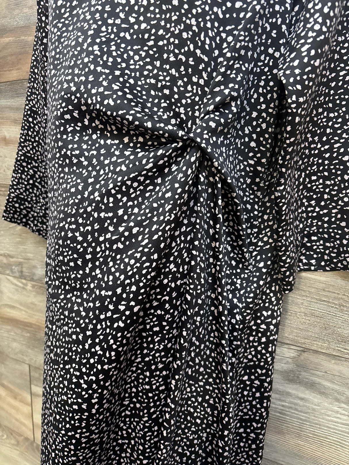 Front close up of Hatch Maternity Lauren dress showing side twist knot and black speckled print on wood background
