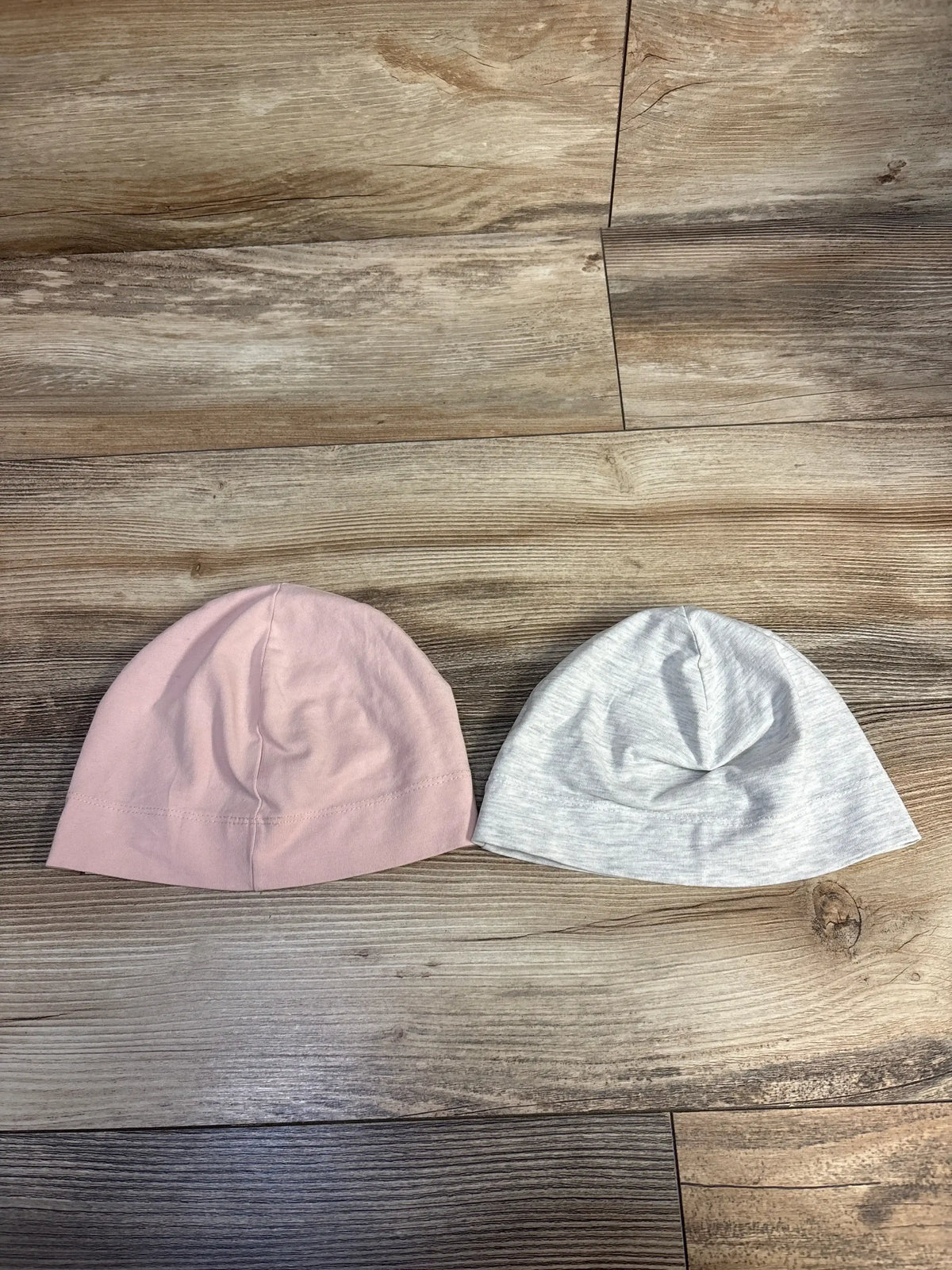 Pink and gray baby hats on wood floor, infant beanies, soft cotton accessories