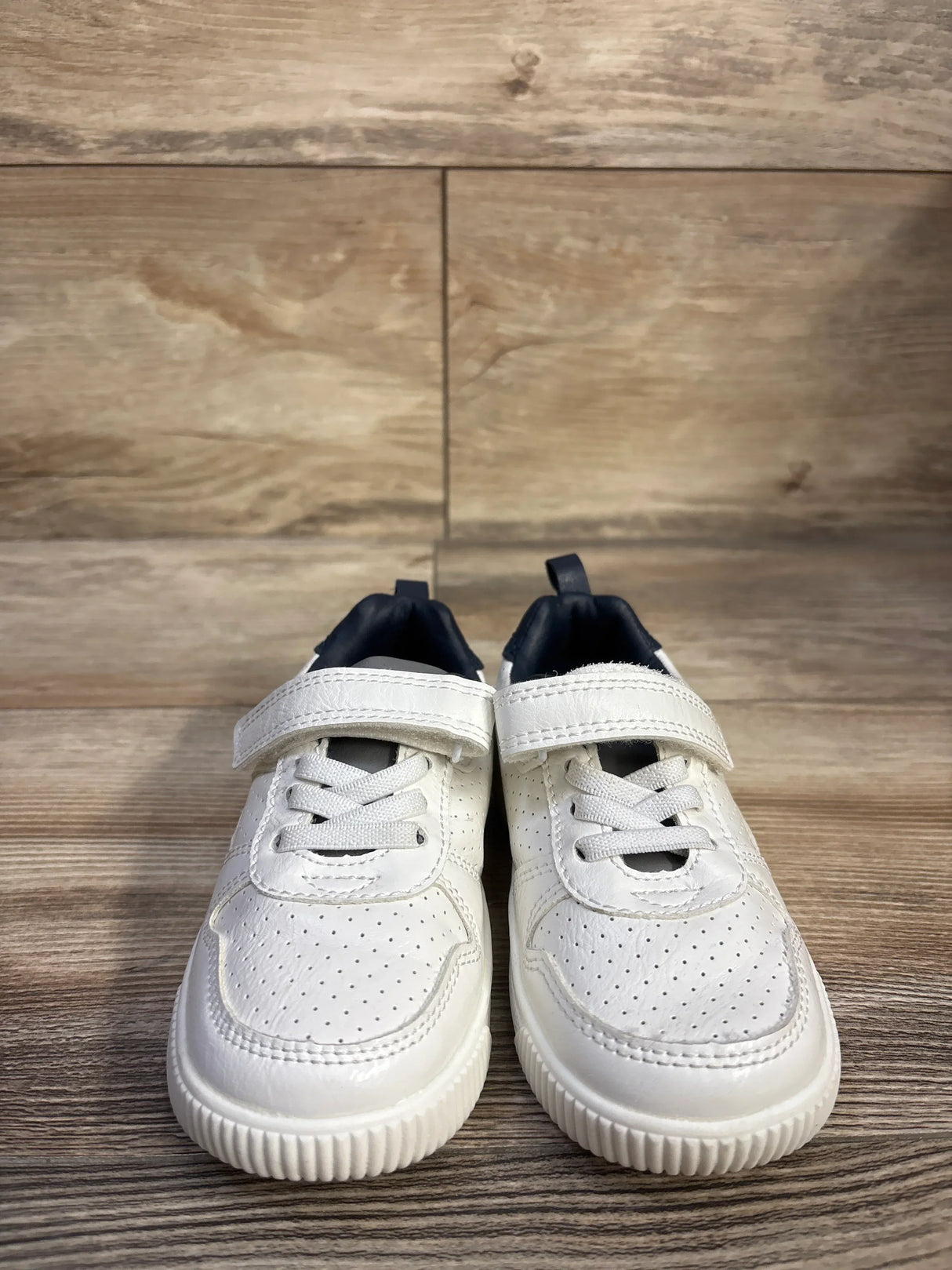 Front view of Carter's Every Step Port sneakers in white with perforated toe, Velcro strap and elastic laces on wood floor
