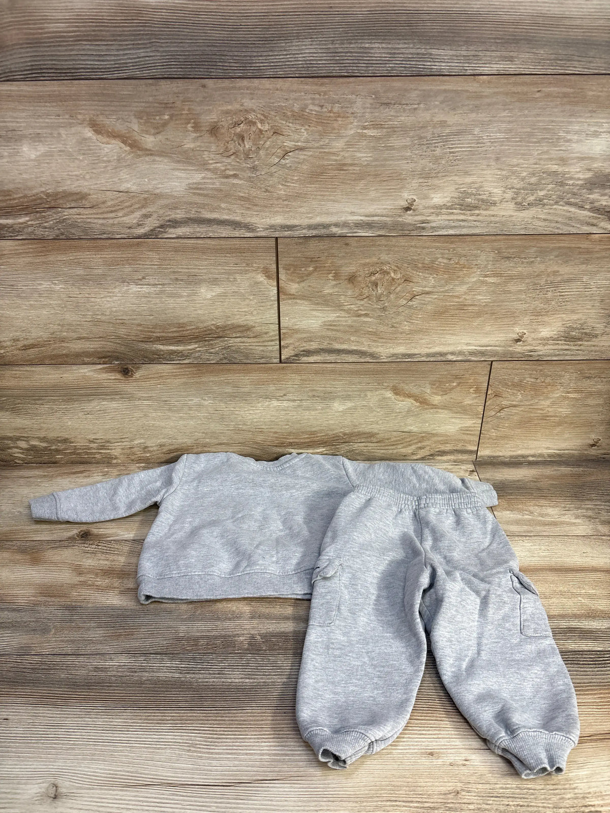 Top view of Champion grey pullover hoodie and joggers set showcasing elasticated cuffs and waistband on a wood background