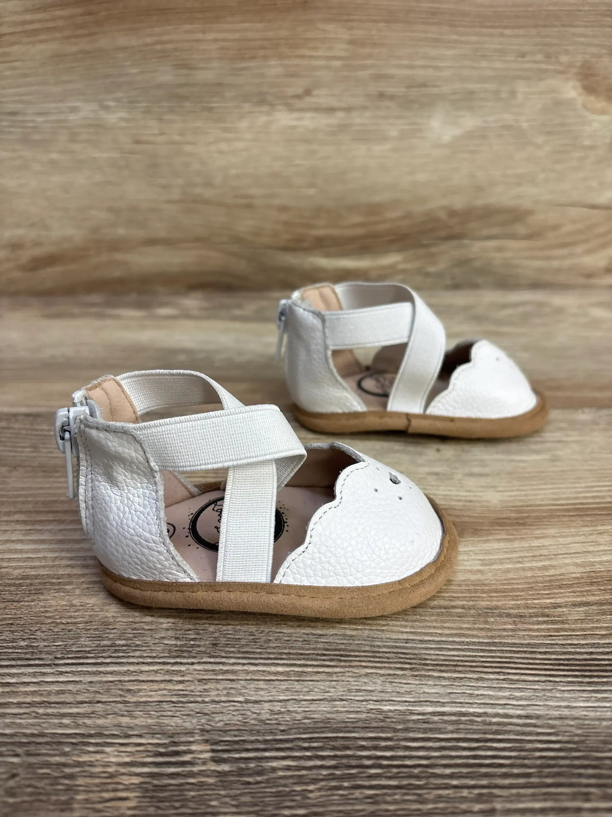 Angled front view of Little Love Bug Sophia white toddler shoes with scalloped toe, elastic cross straps and back zipper