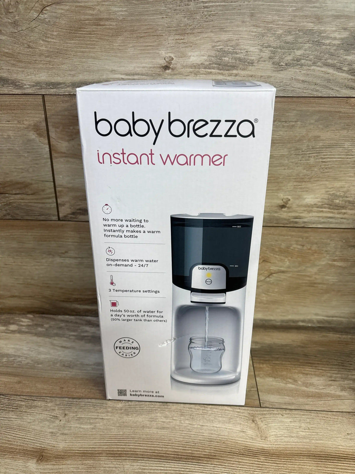 Front view of Baby Brezza Instant Warmer box showcasing sealed retail packaging with product illustration on wood plank floor