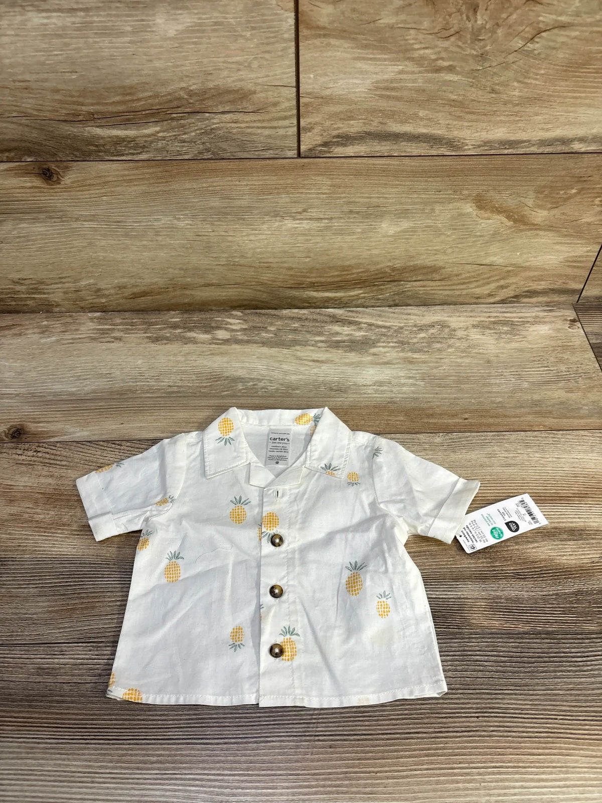Front view of a white newborn Just One You pineapple button-up shirt showcasing short sleeves and button front on a wood background
