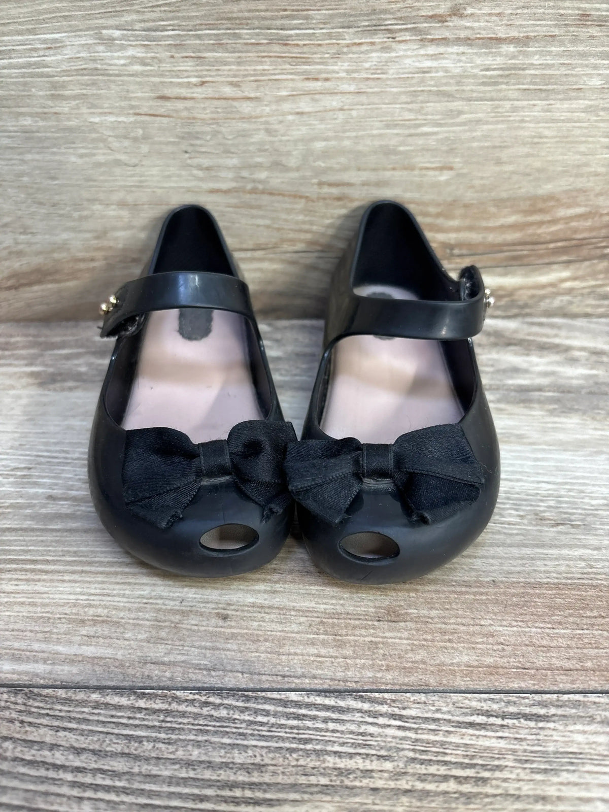 Front view of toddler black jelly Mary Jane flats size 8 showcasing fabric bows and round toe cutouts on wooden surface
