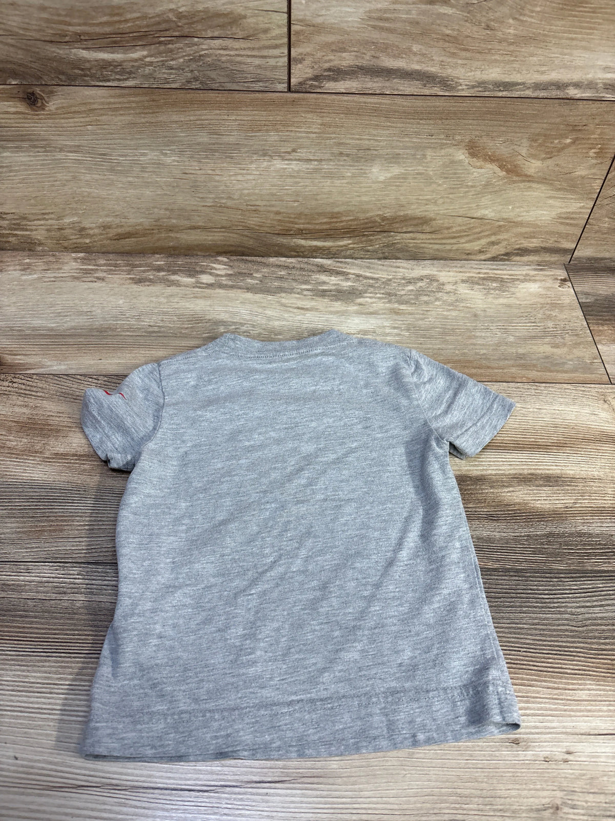 Back view of grey Nike toddler t-shirt (size 2T) showing plain back and small red swoosh on left sleeve on wood floor