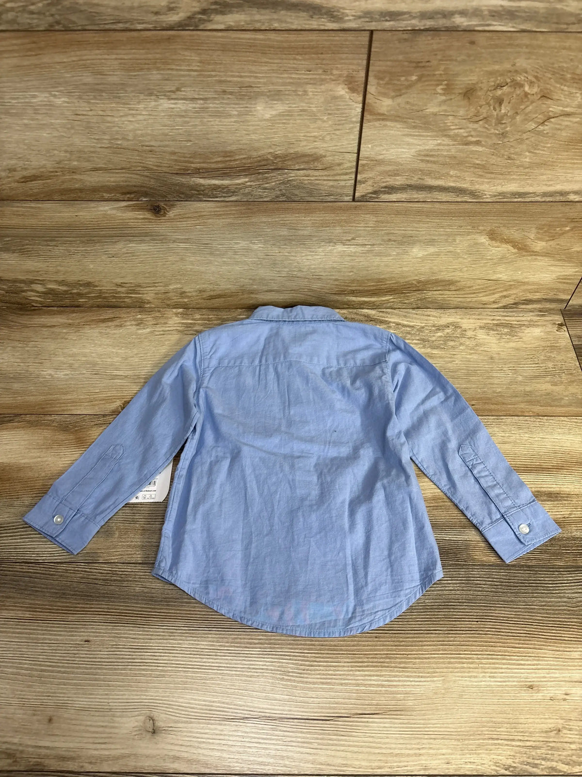 Back view of light blue button-up high-low toddler shirt showcasing cuff buttons and curved hem on wooden floor