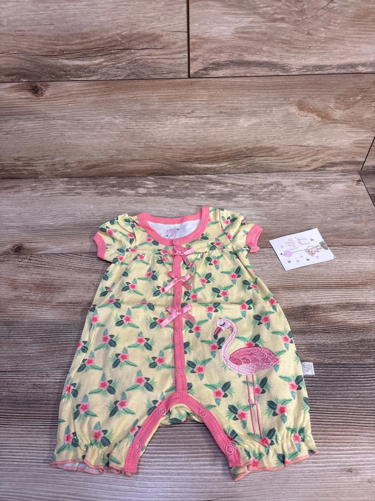 Flat lay of yellow baby shortie romper 0-3M with pink trim, floral print and embroidered flamingo on wood