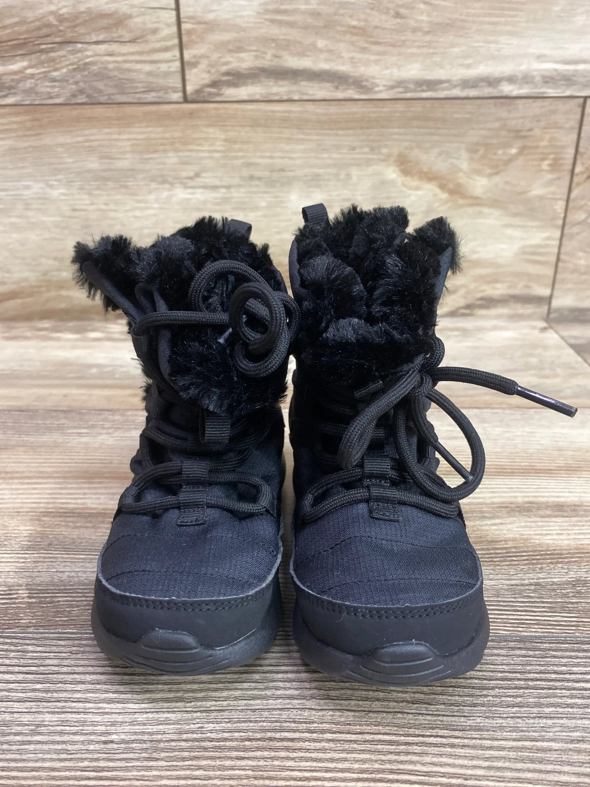 Front view of Nike Roshe One High TDV black winter boots showcasing faux fur lining, drawstring laces, and thick soles on a wood-look floor