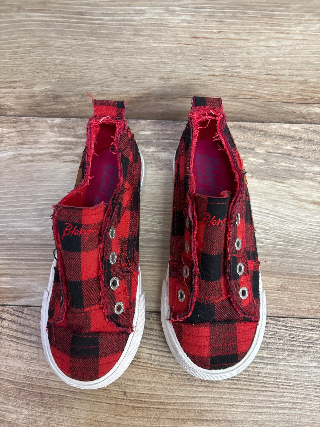 Pair of red and black plaid kids slip-on sneakers with white soles on wooden floor