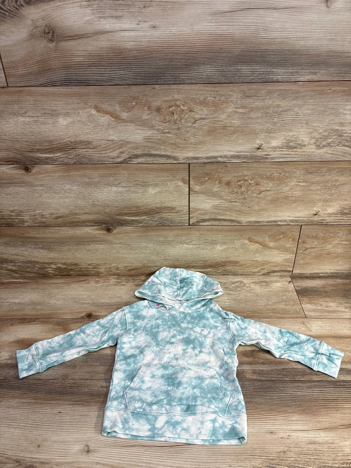 Kids blue and white tie-dye hoodie with front pocket, laid flat on wood floor