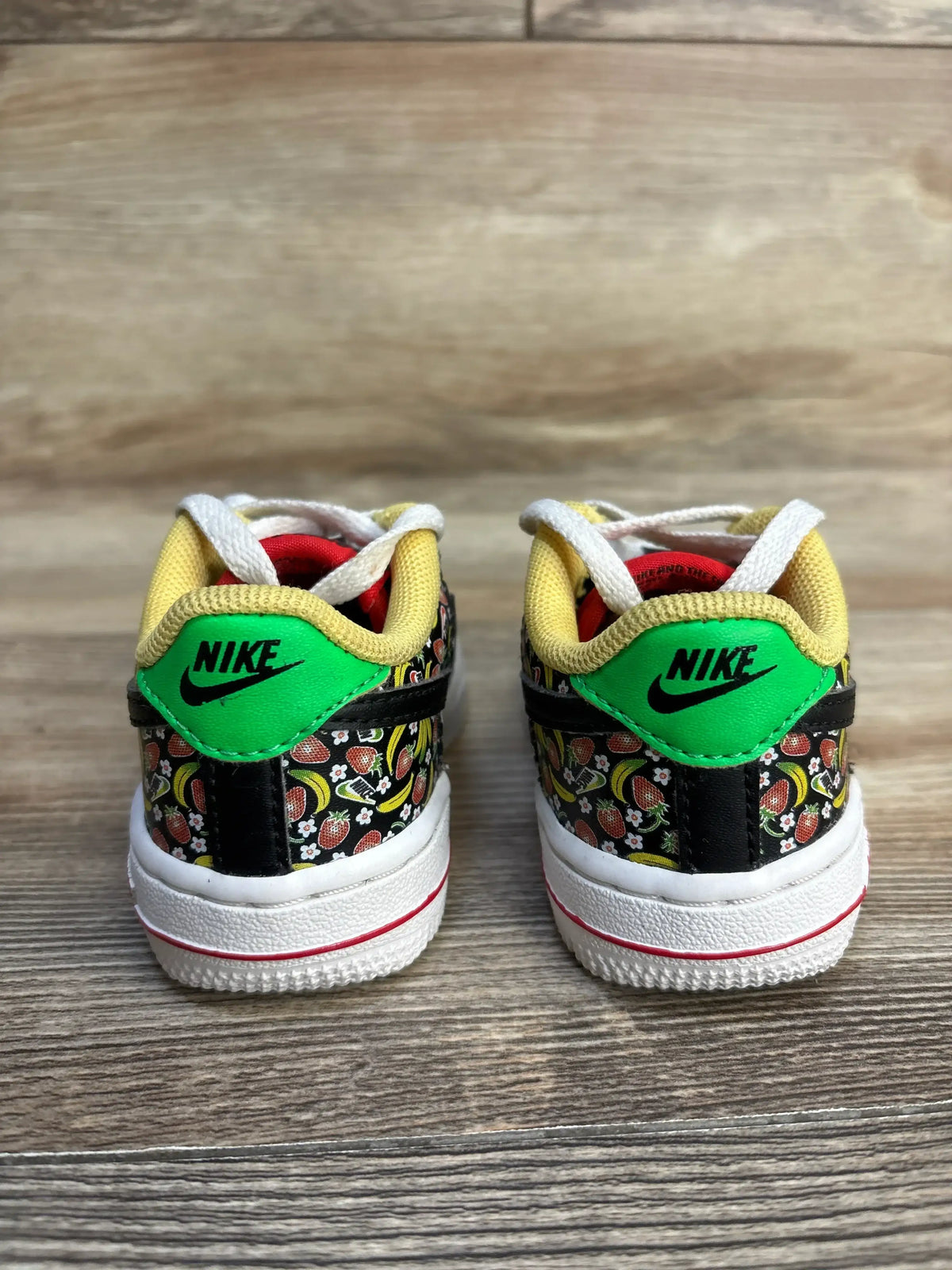 Nike toddler sneakers with fruit print, green heel tab, white laces, and red sole on wood floor