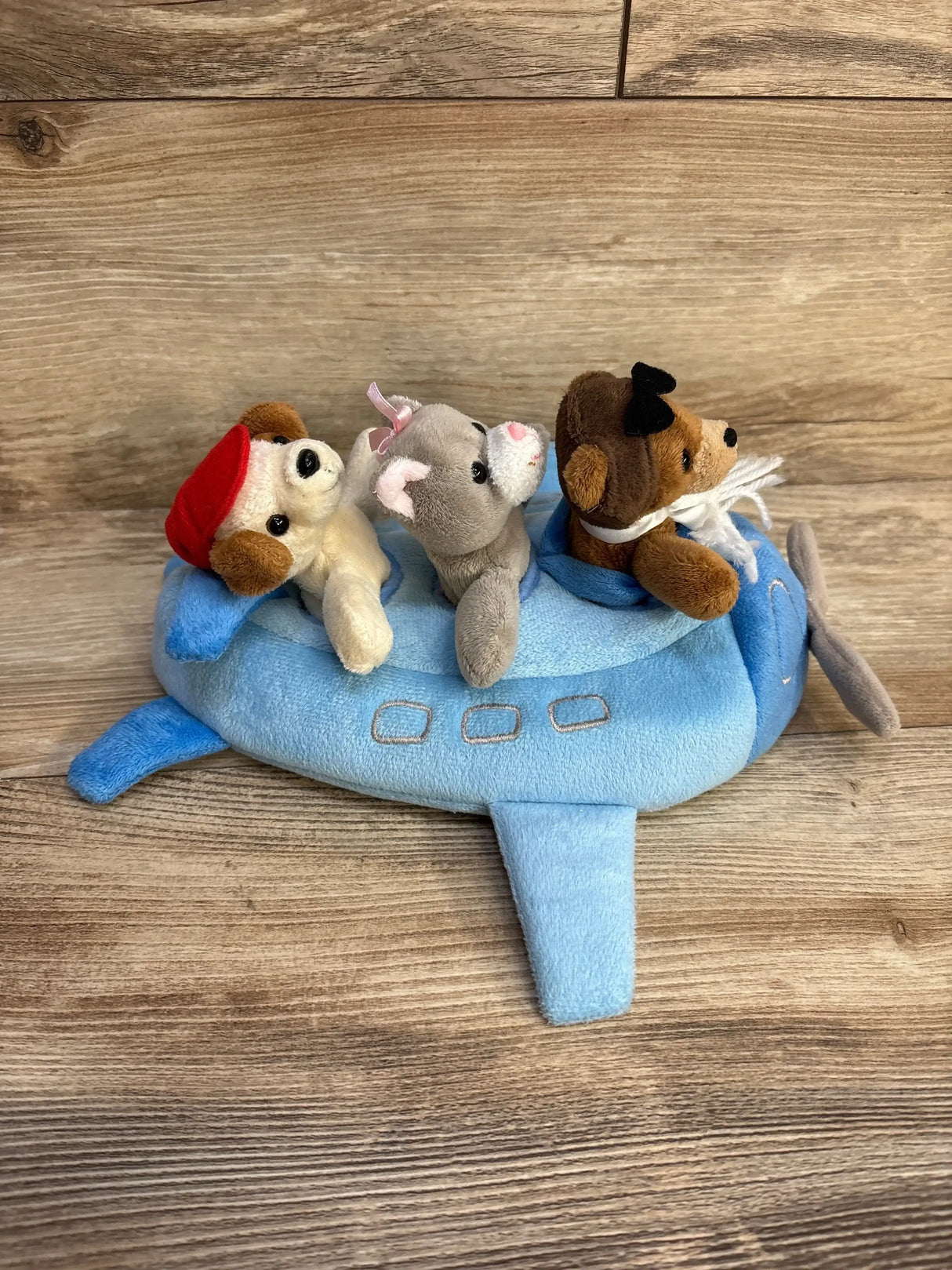 Angled view of 10-inch blue plush airplane with three removable animal finger puppets on wood background