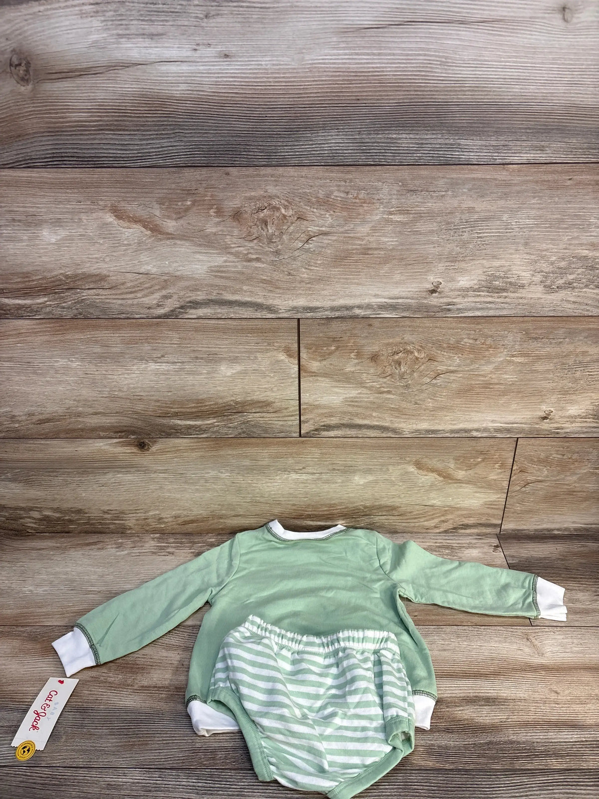 Green long sleeve baby shirt with white cuffs and matching striped bloomers on wood background