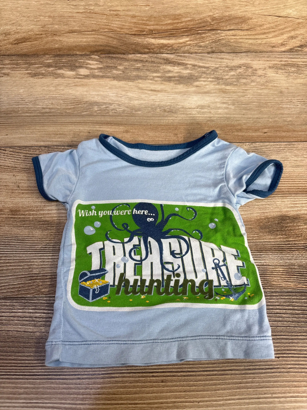 Front view of blue Kickee Pants bamboo treasure hunting shirt with TREASURE hunting octopus graphic on wooden background
