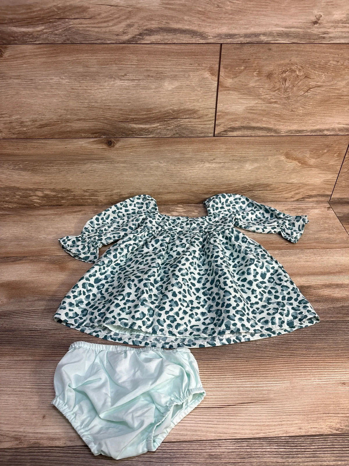 Flat lay of two-piece leopard-print twill dress with smocked bodice, puff sleeves, matching light blue bloomers on wood floor