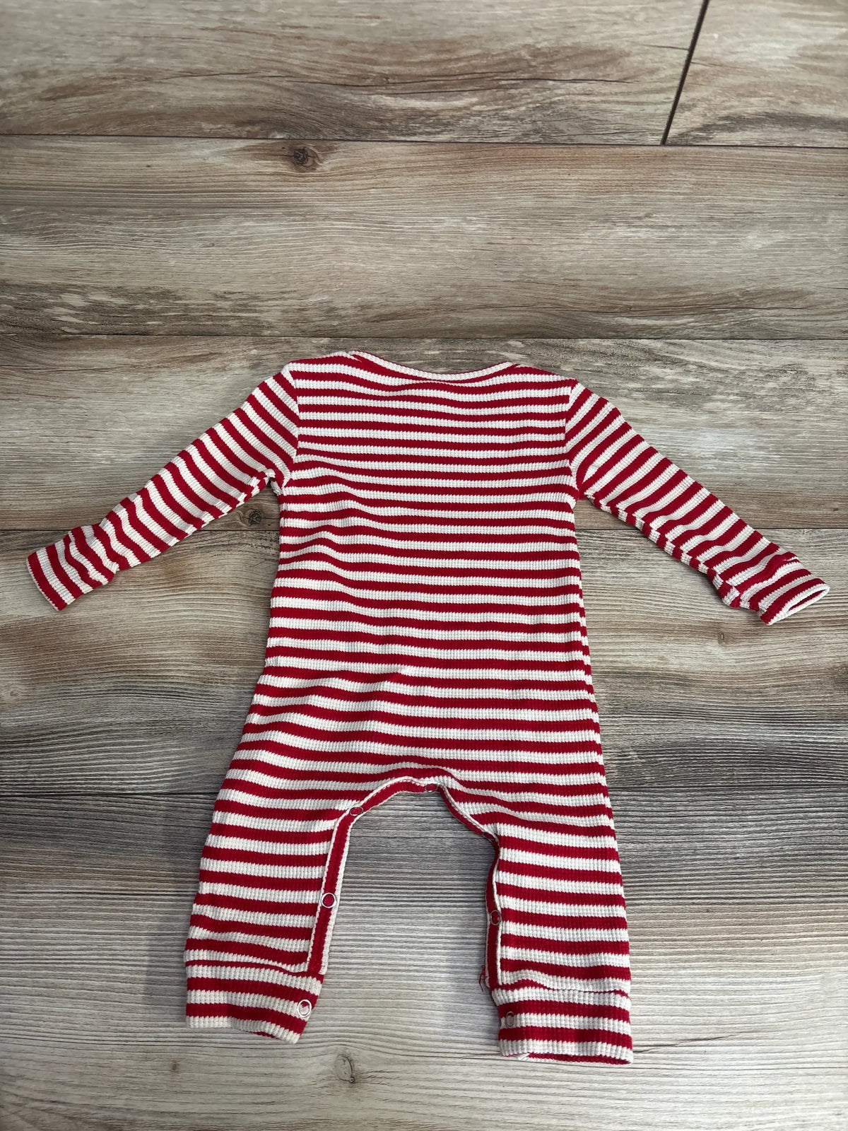 Red and white striped long-sleeve baby romper with snap buttons on gray wood floor