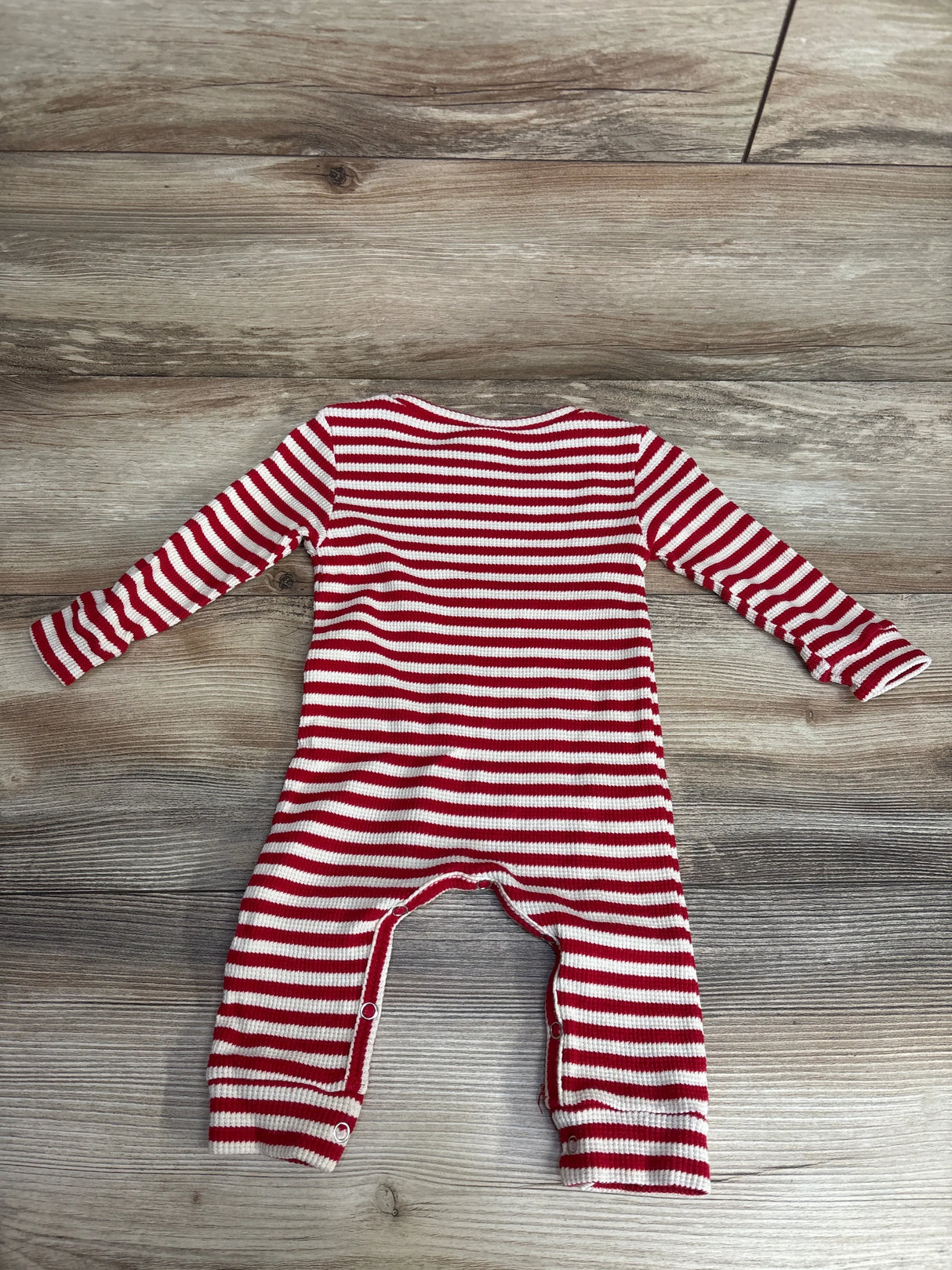 Red and white striped long-sleeve baby romper with snap buttons on gray wood floor