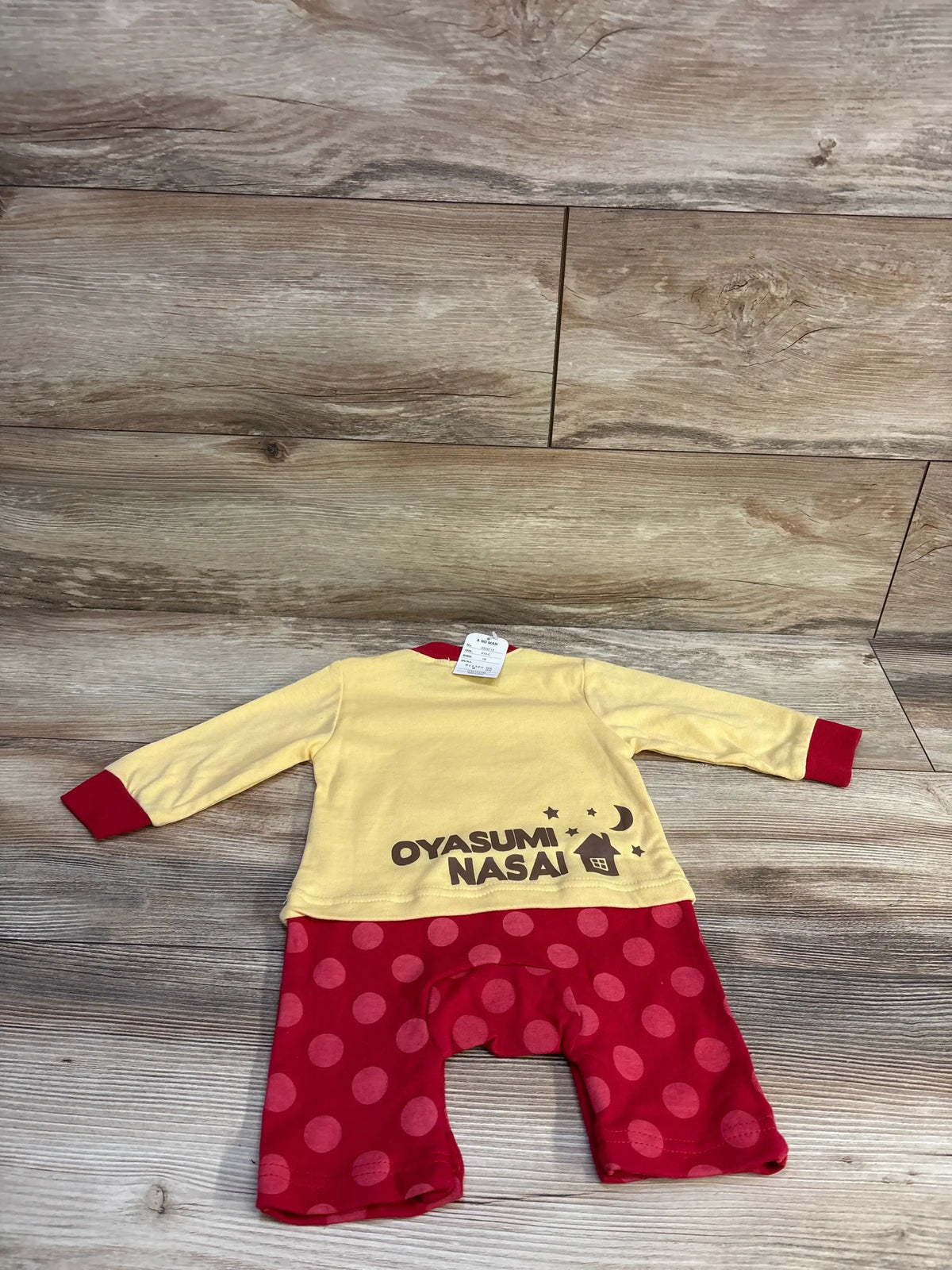 Back view of yellow baby coverall with red cuffs and red polka dot legs, showing OYASUMI NASAI print on wood floor
