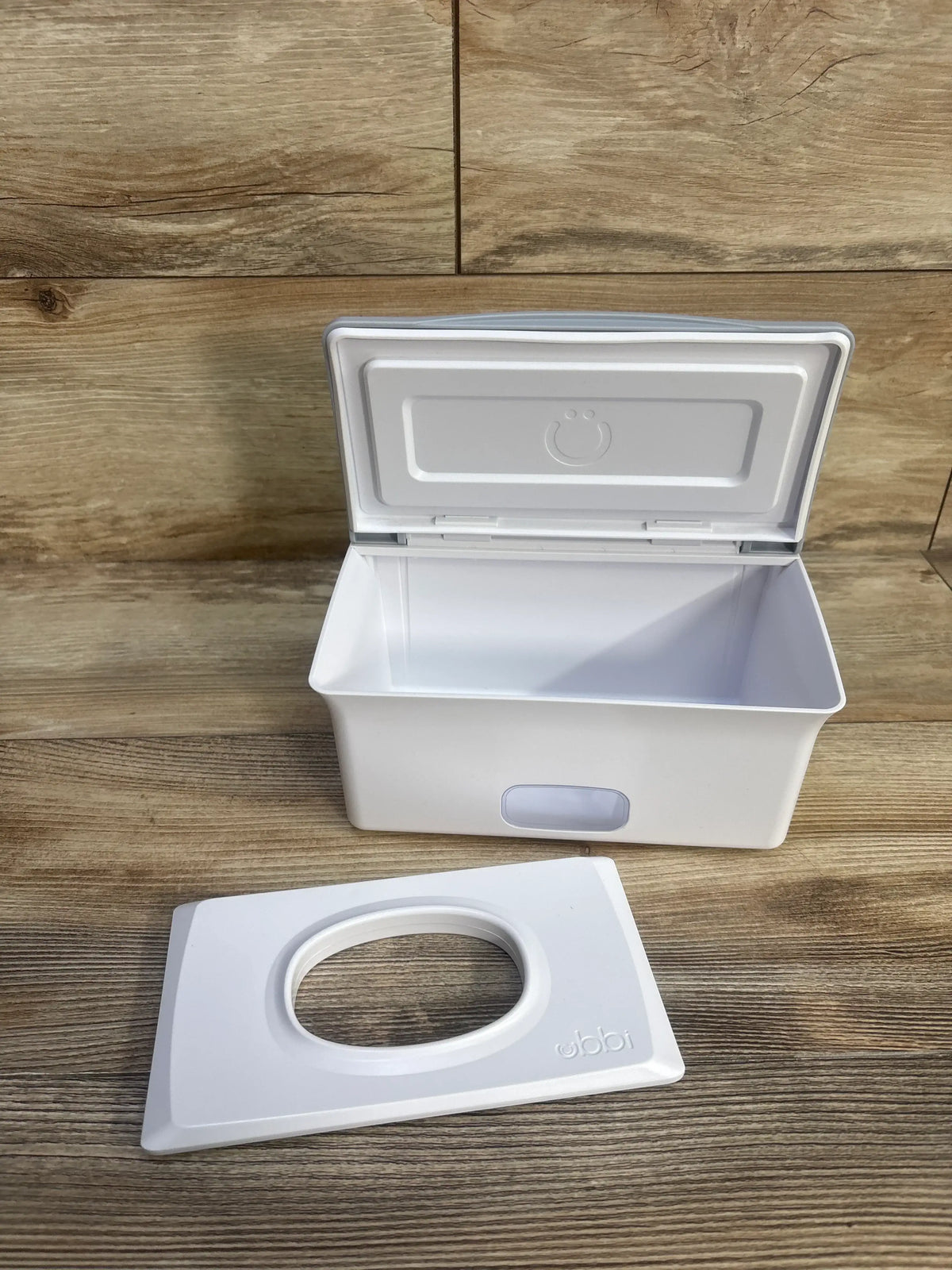 Open view of Ubbi grey wipes dispenser showcasing its interior and lid on a wood-look background