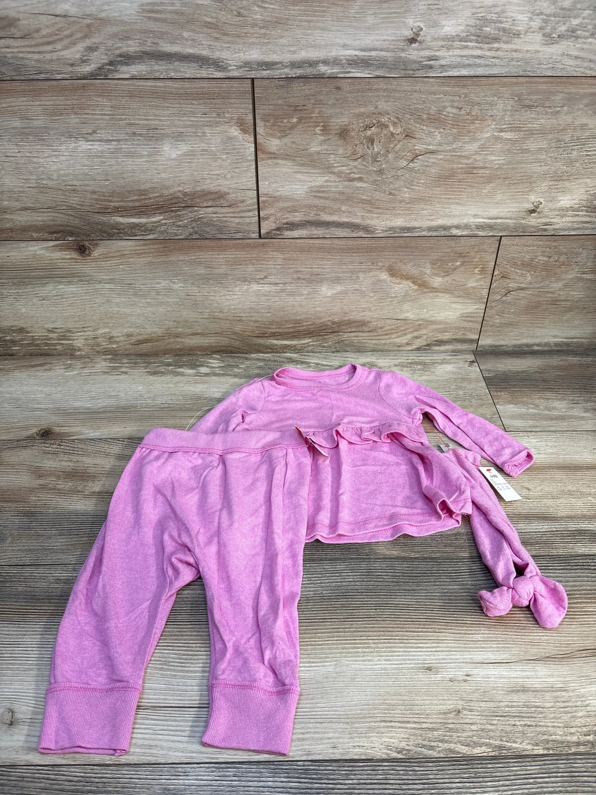 Pink toddler outfit set with long sleeve shirt, pants, and matching knotted hat on wood floor