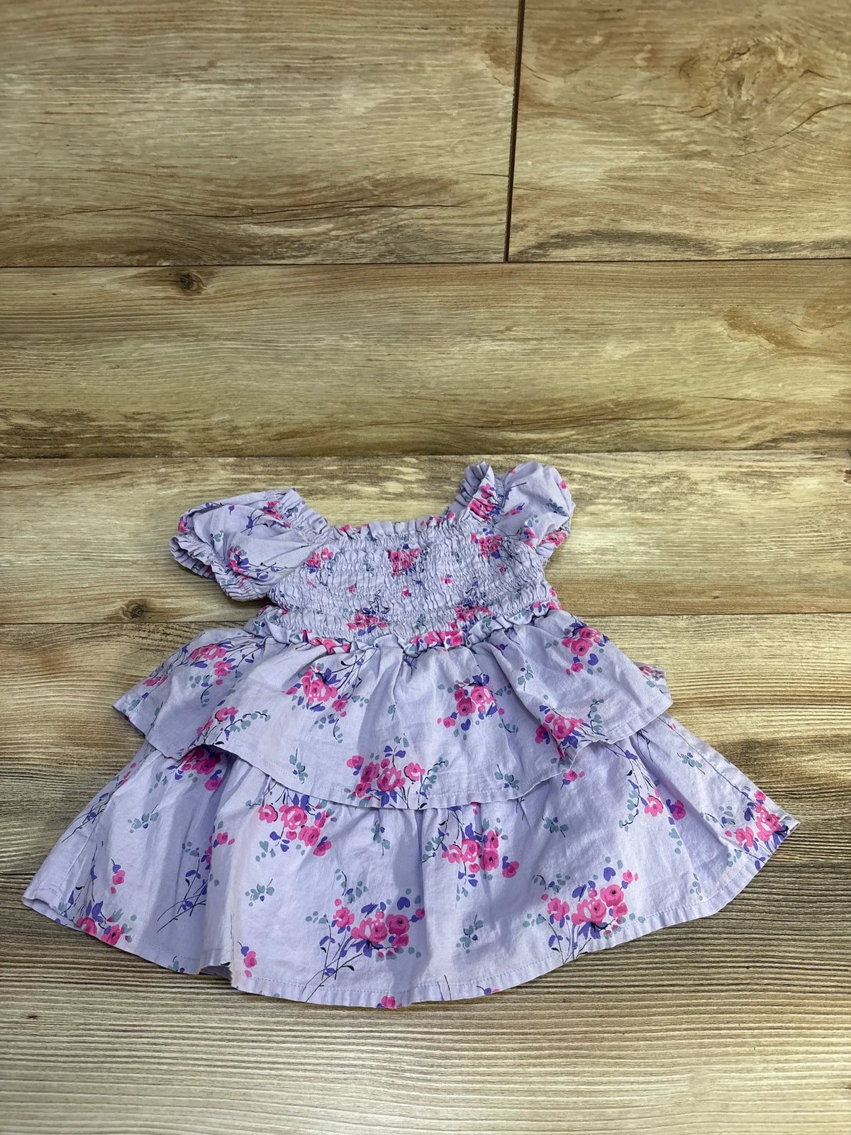 Flat lay of purple Baby Gap baby dress with smocked bodice, puff sleeves, tiered ruffle skirt, and pink floral print on wood background