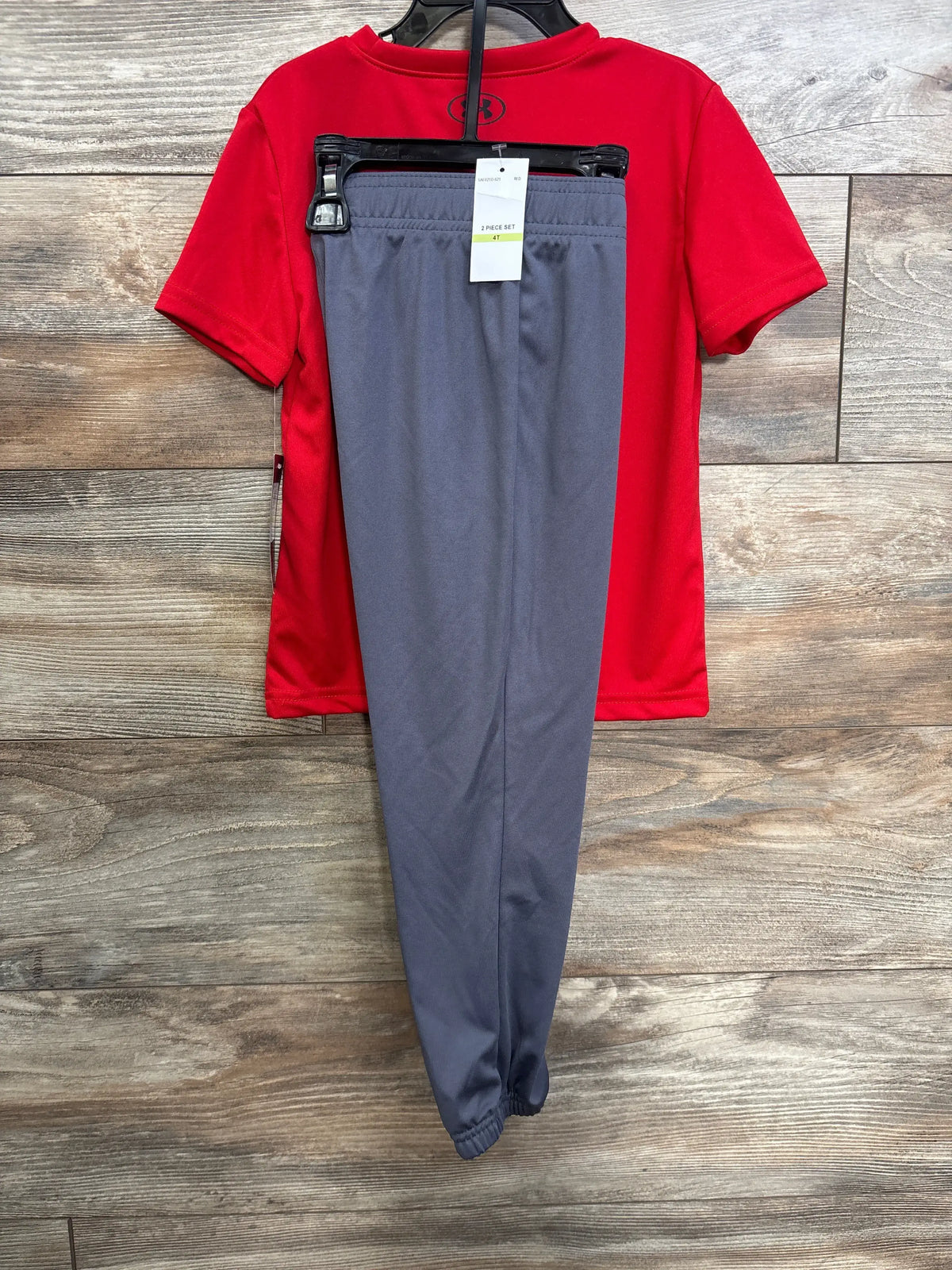 Back view of Under Armour toddler 2-piece set with red shirt and small UA logo, gray elastic-waist pants on wood background