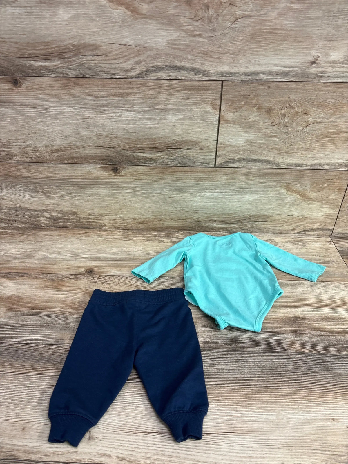 Flat lay of two-piece baby set: long-sleeve turquoise bodysuit with snap crotch and navy elastic-waist pants on wood floor