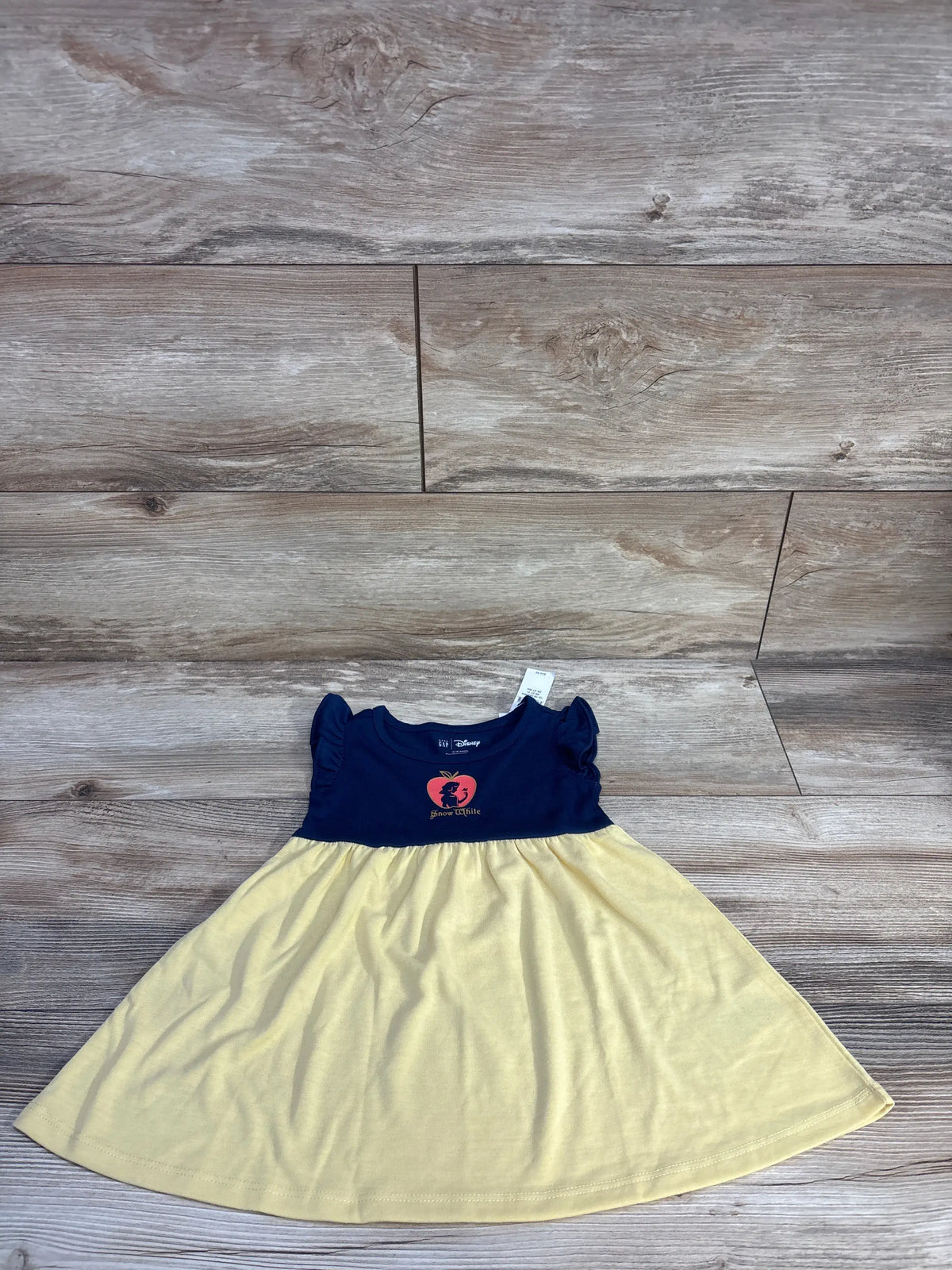 Front view of Baby Gap x Disney Snow White PJ dress showcasing navy bodice, yellow skirt, and flutter sleeves on a wood floor