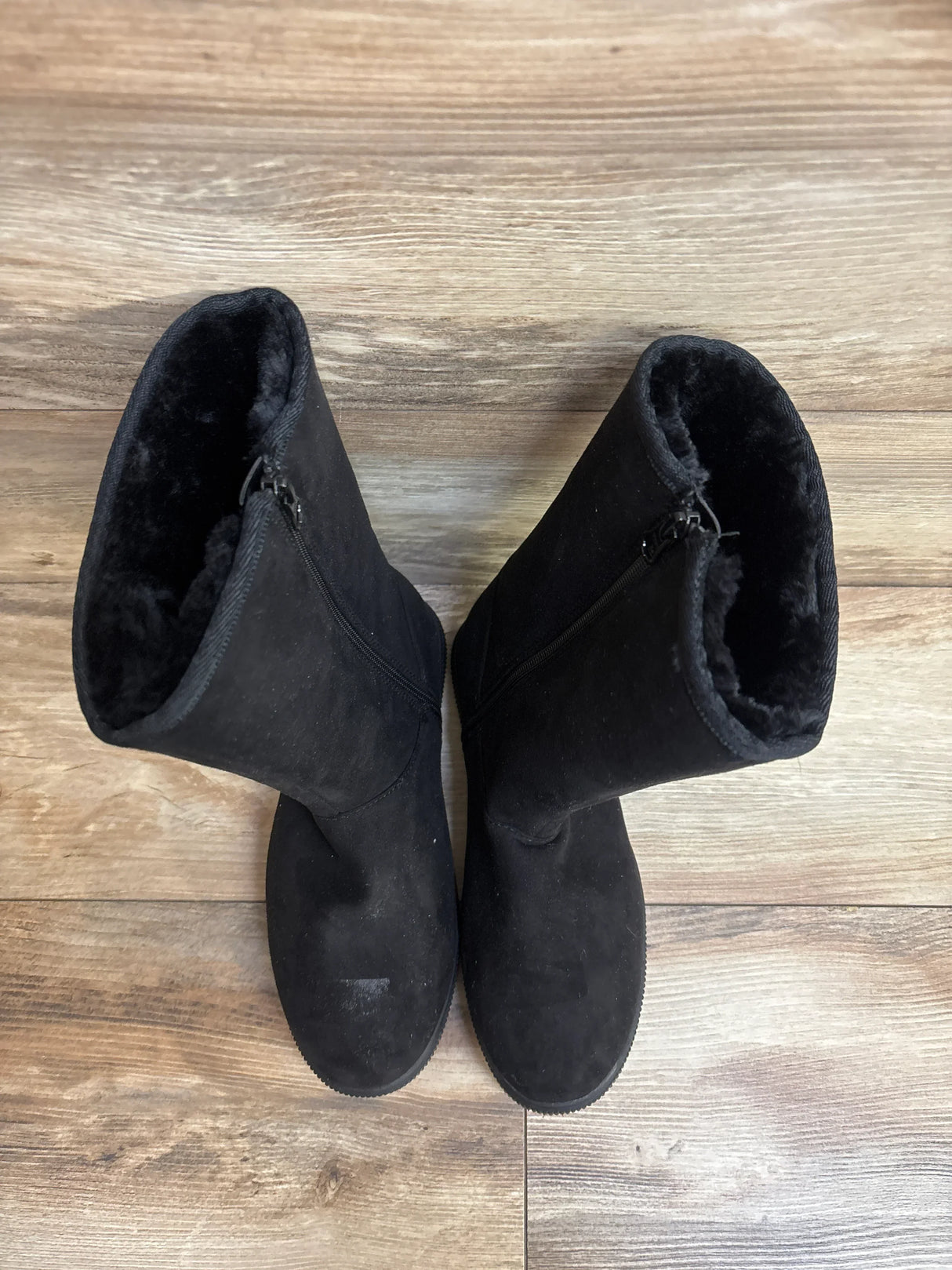 Pair of black suede kids winter boots with zippers, faux fur lining, on wood floor