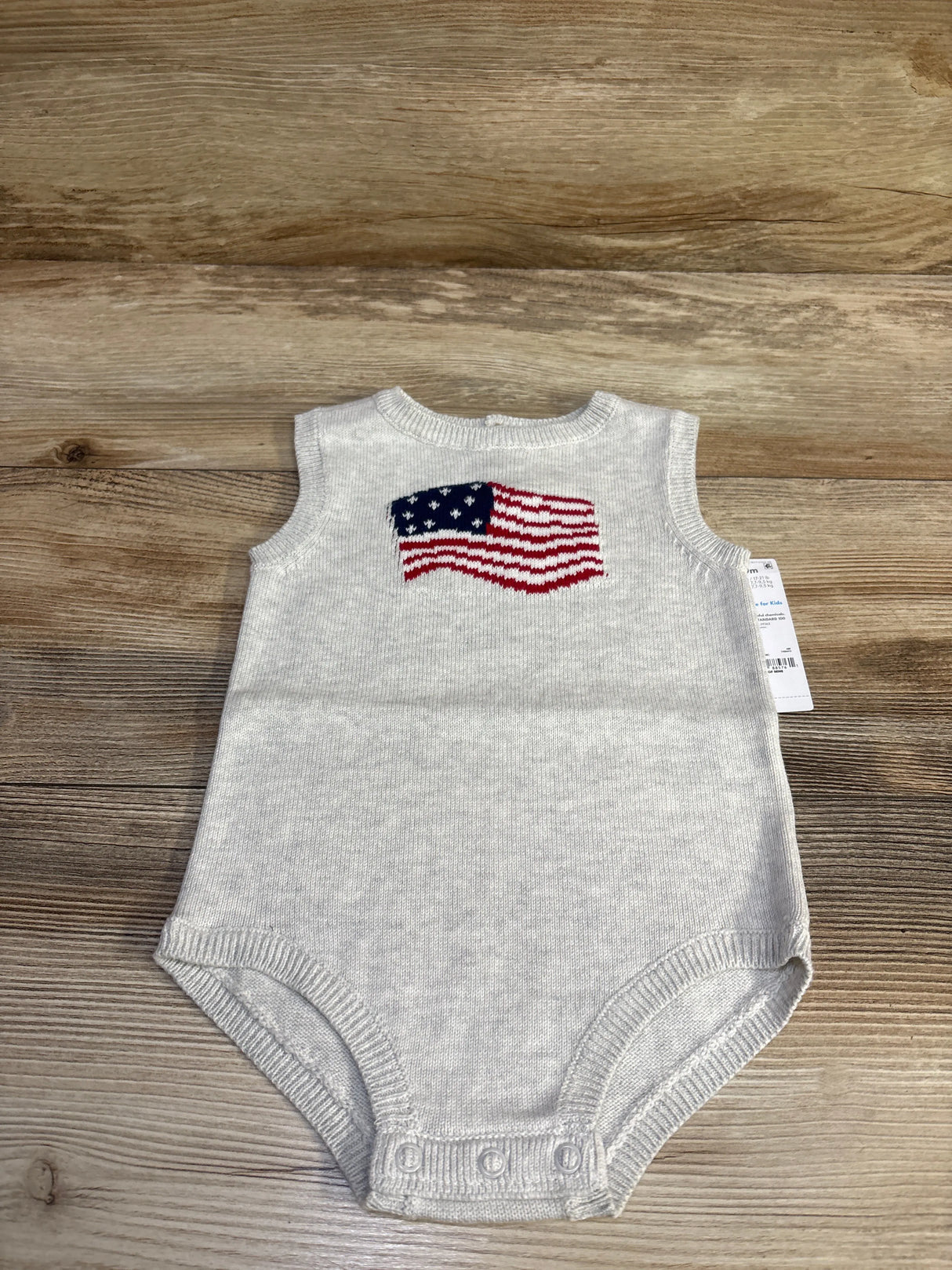 Top-down view of grey Child of Mine knit bubble romper size 6-9 months showcasing American flag intarsia on chest and snap crotch closures on wood background