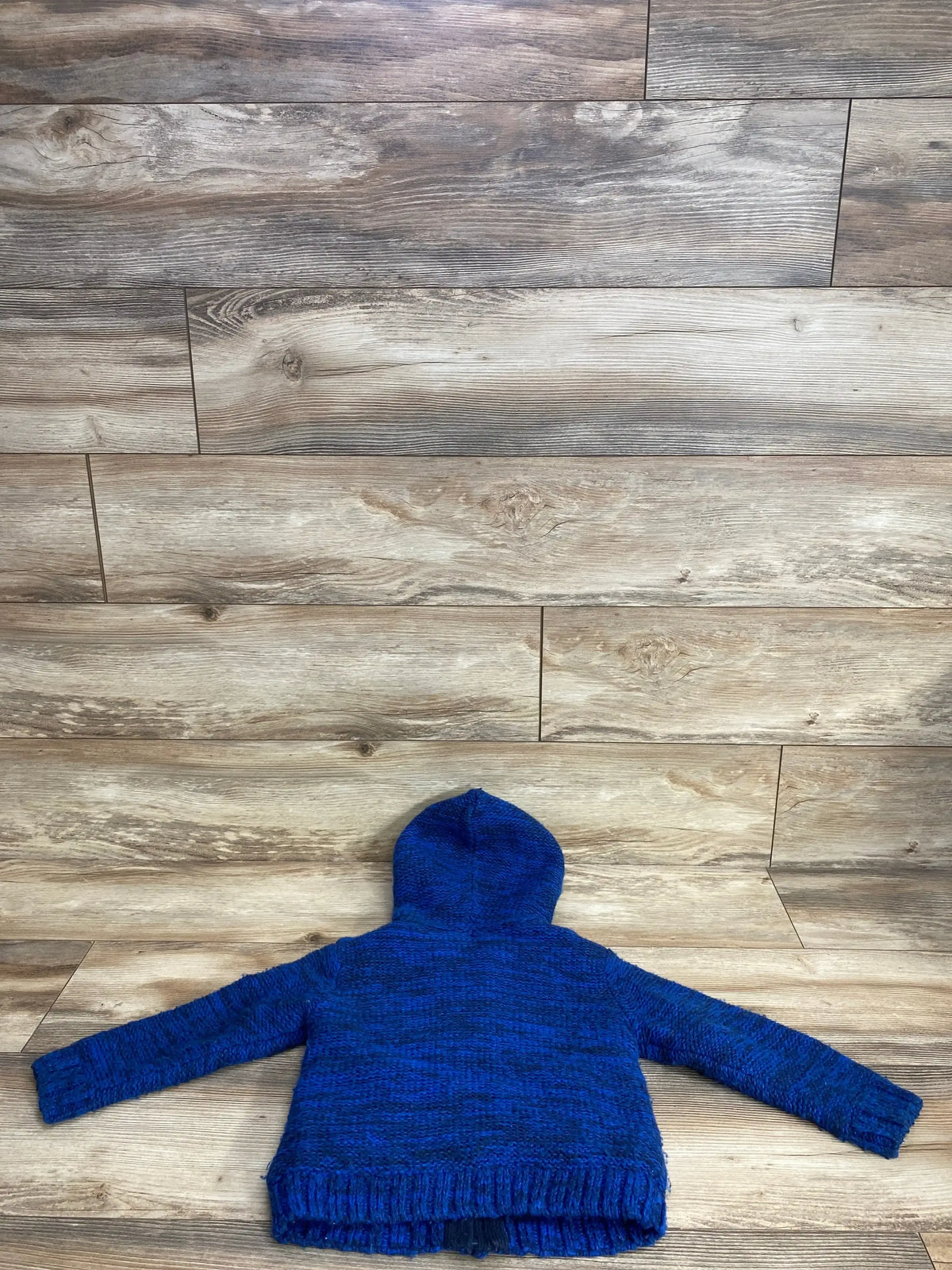 Back view of a blue knitted hooded sweater for kids on wooden floor background