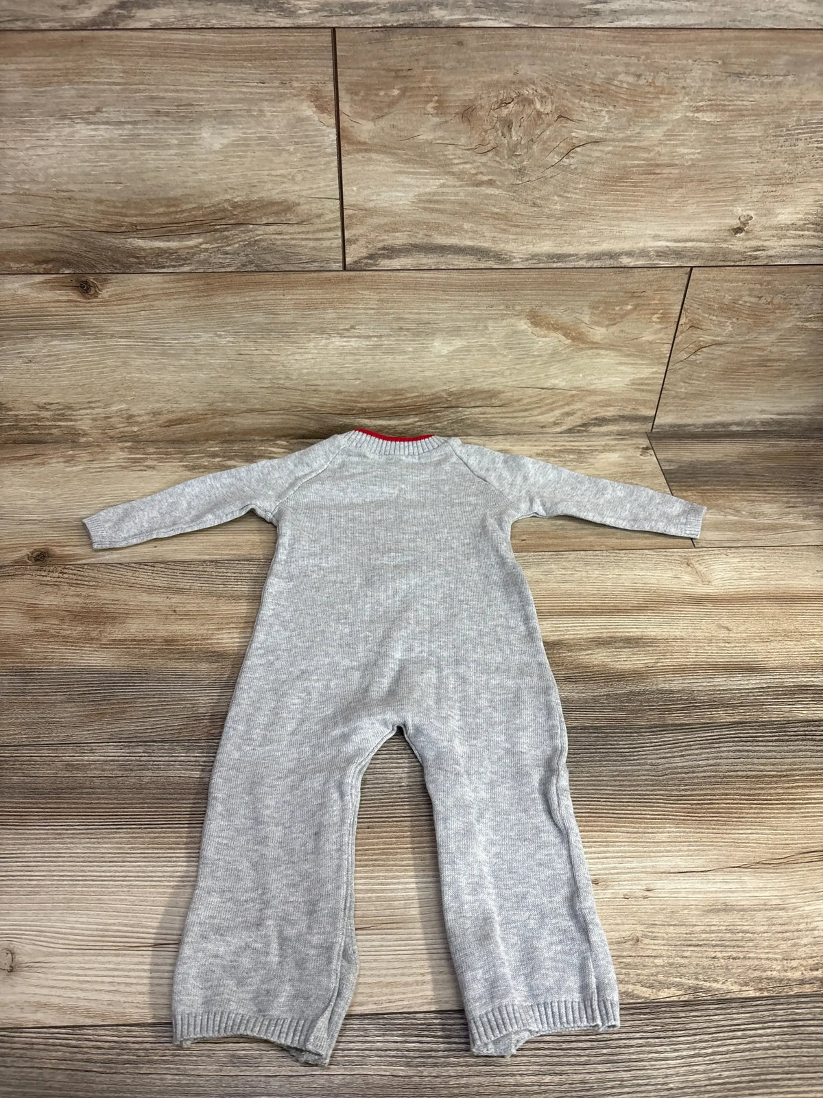 Gray baby onesie with red trim, laid flat on wood floor — cozy infant clothing for newborns