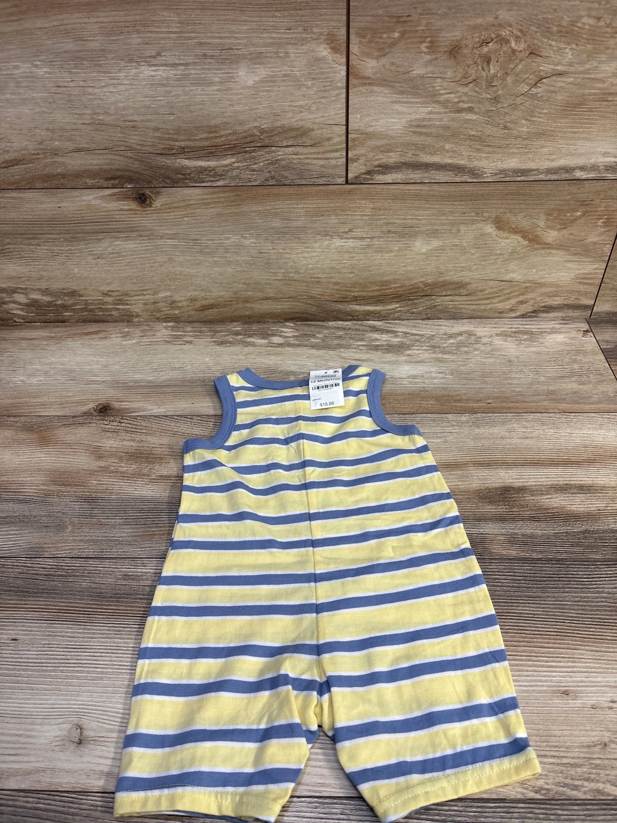 Front flat lay of yellow and blue striped shortie romper showcasing sleeveless design, round neck and contrast blue trim on wood background