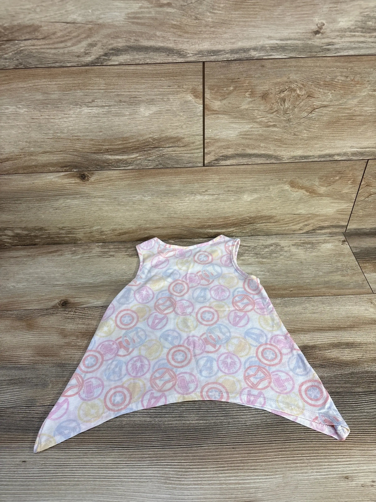 Flat lay of white toddler Avengers flare tank top showcasing handkerchief hem and pastel Avengers logo print on wood background