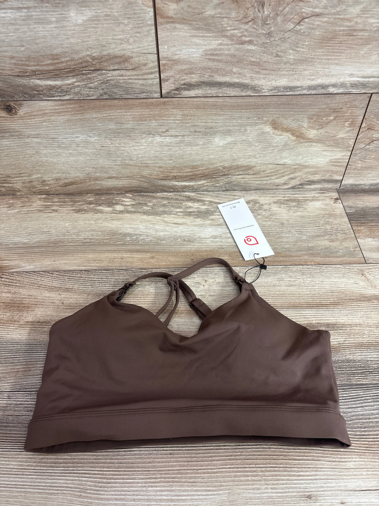 Flat lay of Supportive Flow nursing and pumping sports bra in espresso, size M, V-neck front, crisscross back straps, wide underband on wood