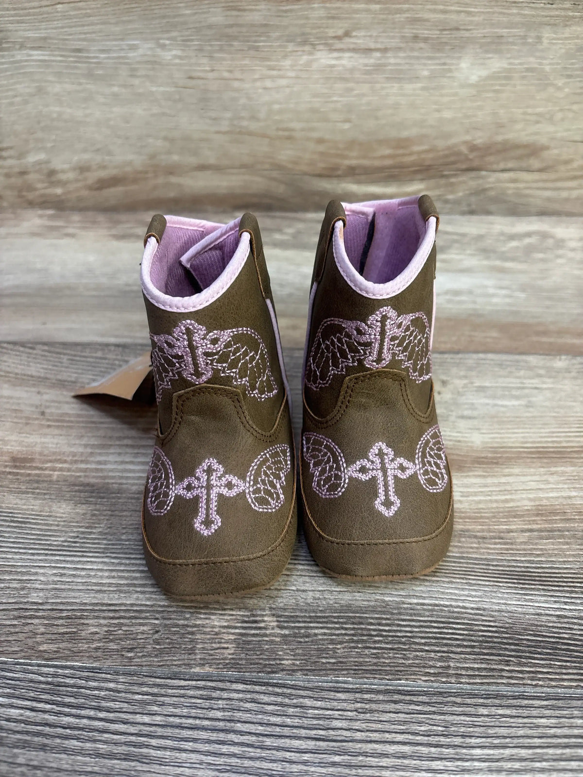 Front view of Twister Gracie baby buckers boots, brown with pink embroidered crosses and wings, size 3C on wood backdrop