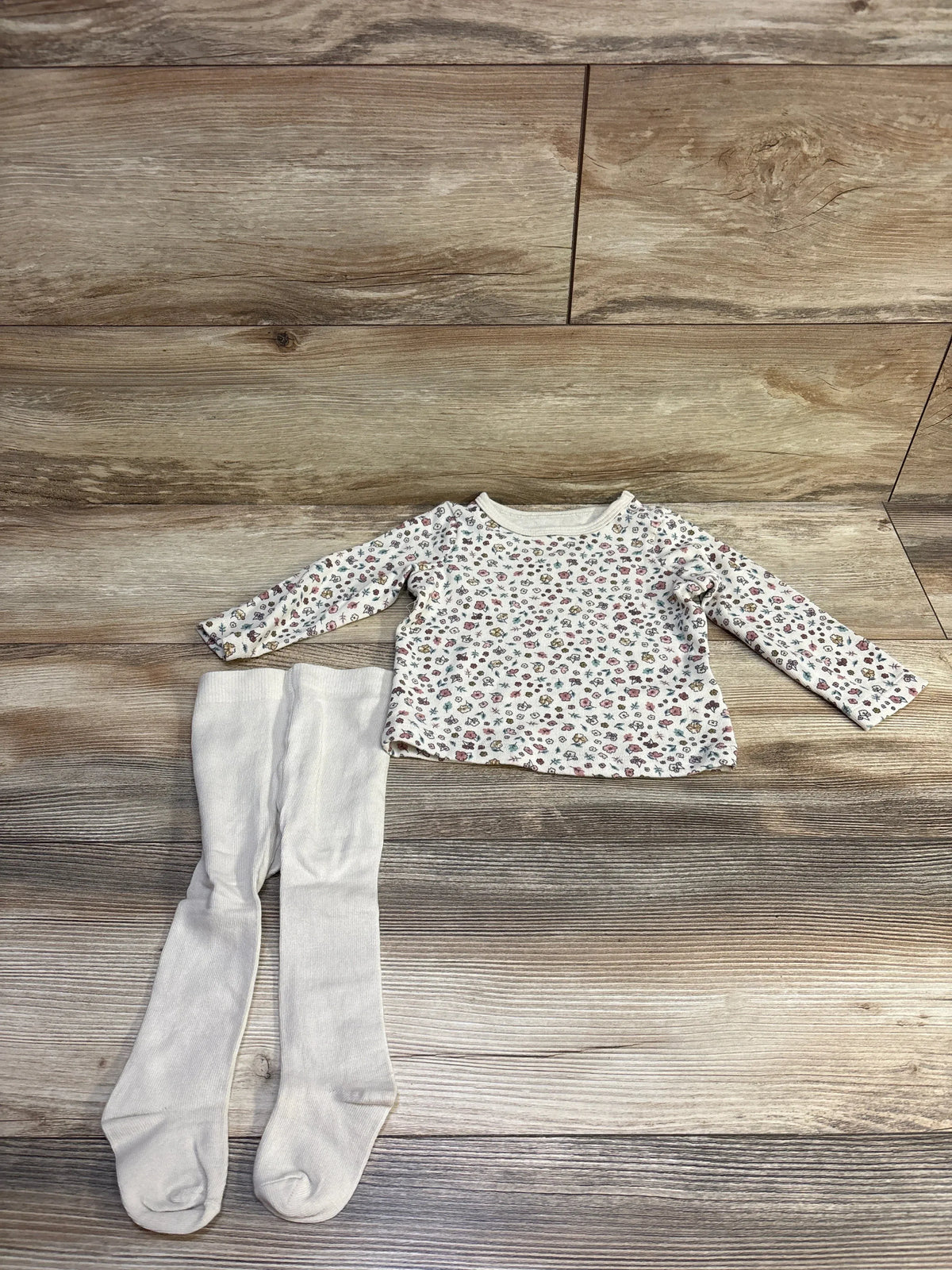 Flat lay of Carter’s 2-piece floral long-sleeve shirt and beige footed tights, size 9 months, on wood plank background