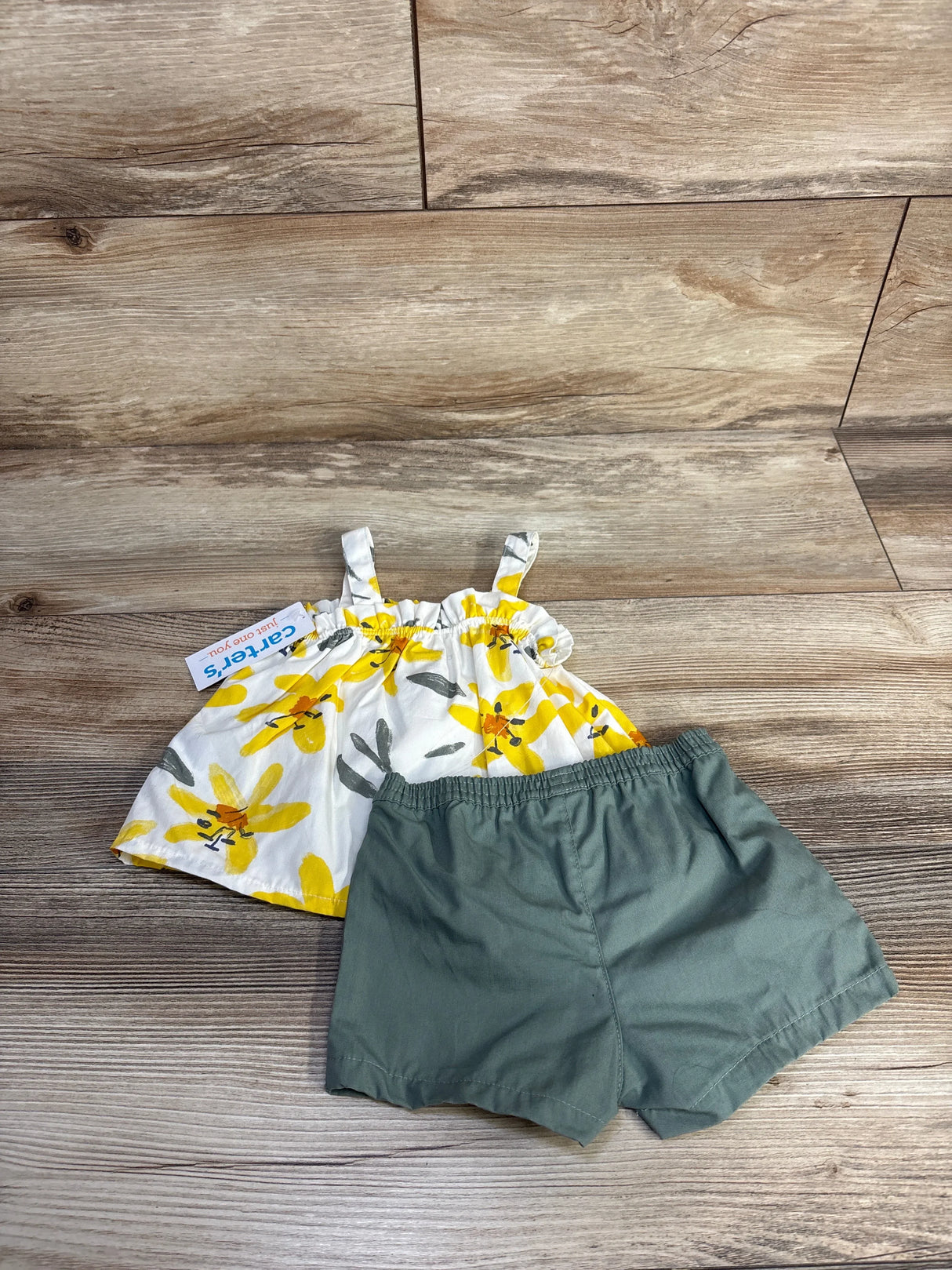 Flat lay of baby 2-piece set showing white button-front floral top and green elastic-waist shorts on wood background