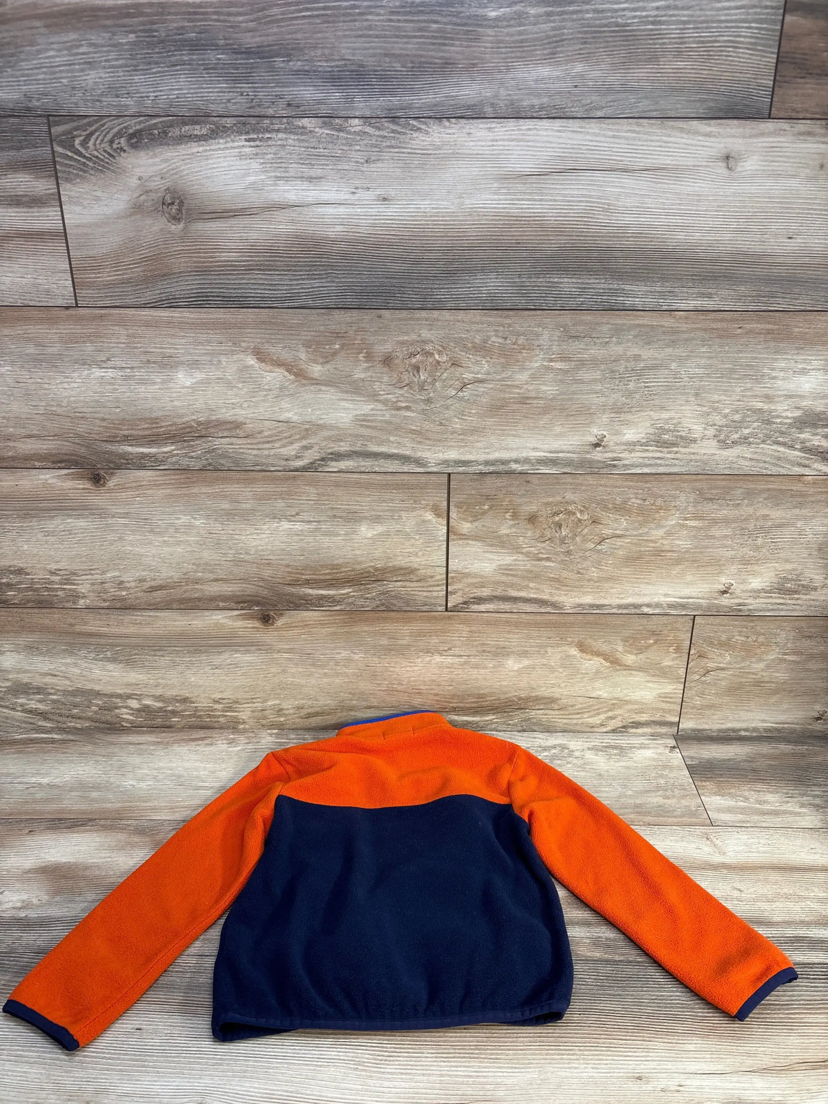Back of Ralph Lauren colorblocked fleece pullover, 5T, orange sleeves and yoke with navy lower back on wood floor