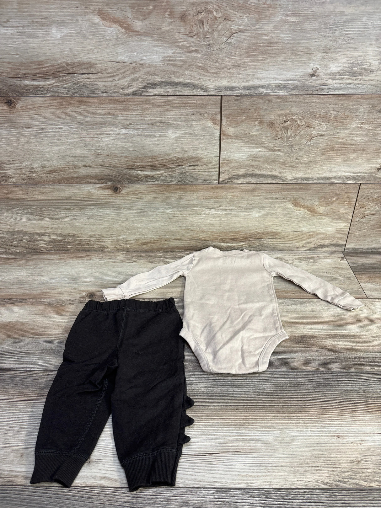 Flat lay beige long-sleeve bodysuit and black pants with three ruffle spikes on outer leg, 9M, on wood background