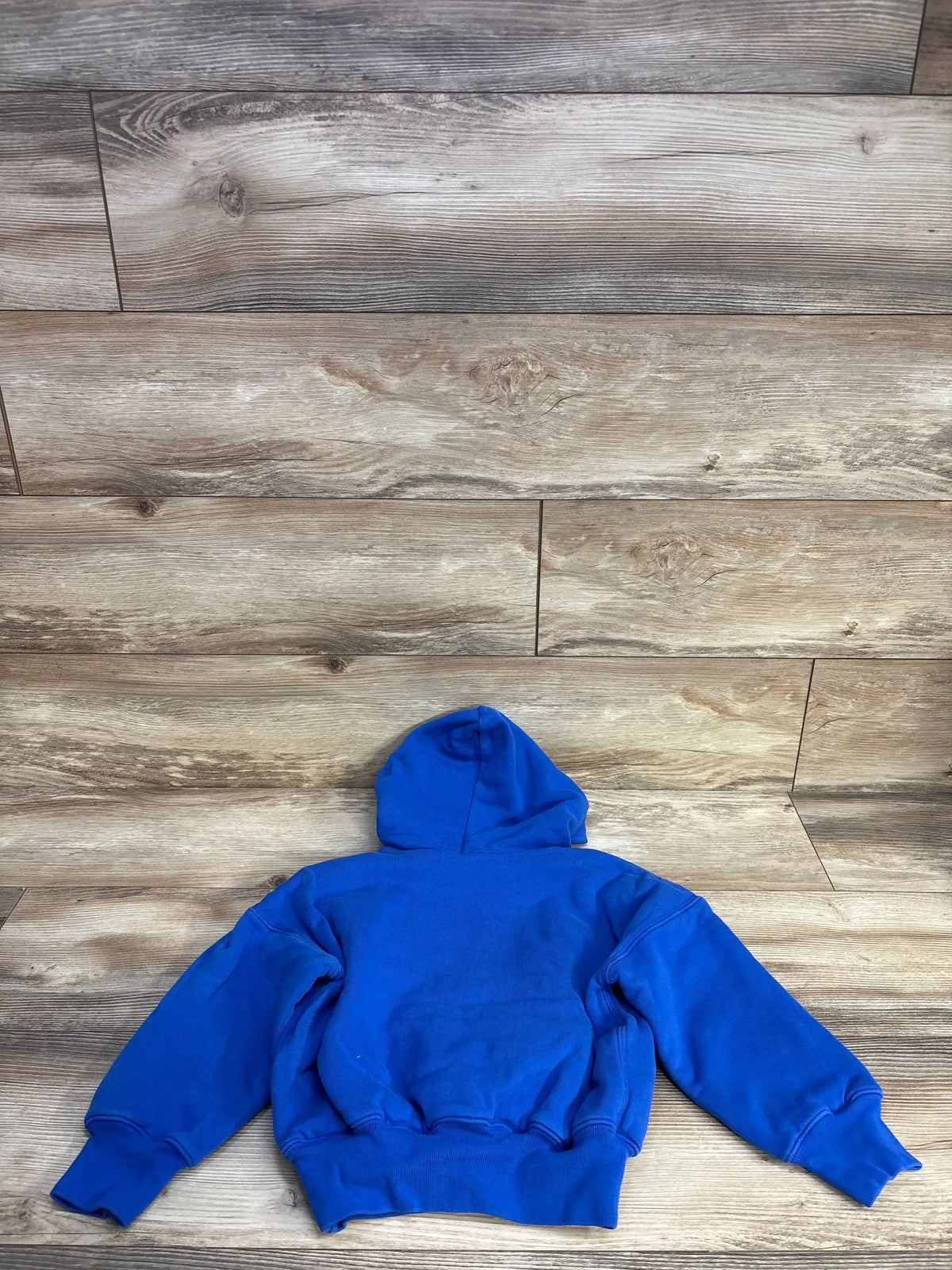 Blue hoodie sweatshirt laid flat on wood floor, back view, casual clothing
