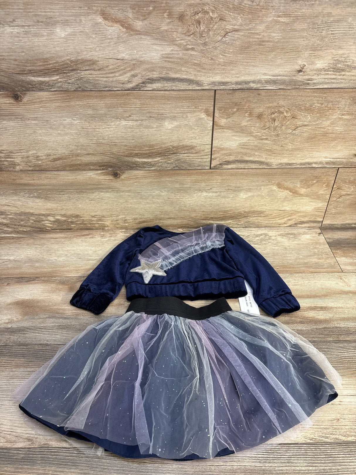 Top-down view of Samara navy velvet top and matching tulle skirt showing star applique and glittery tulle on wood background