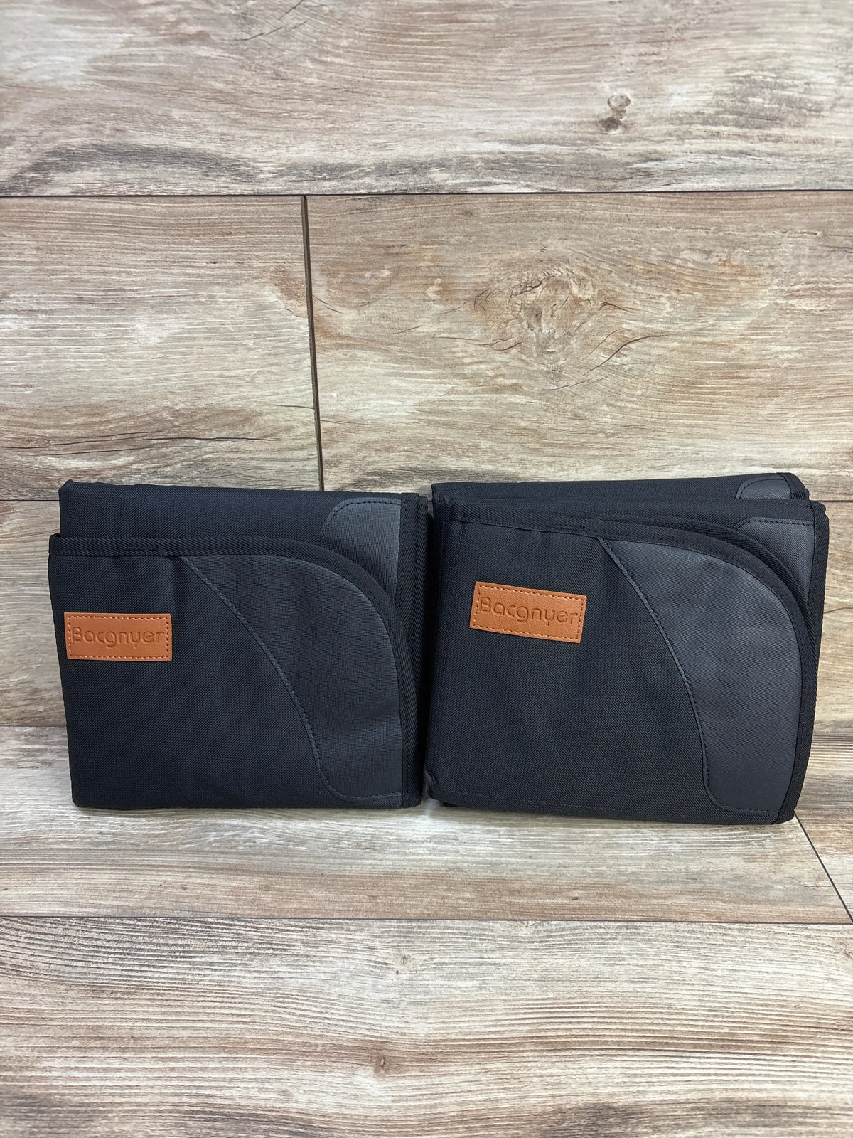 Two black Bacgnyer car seat protectors side by side on a light wood surface.