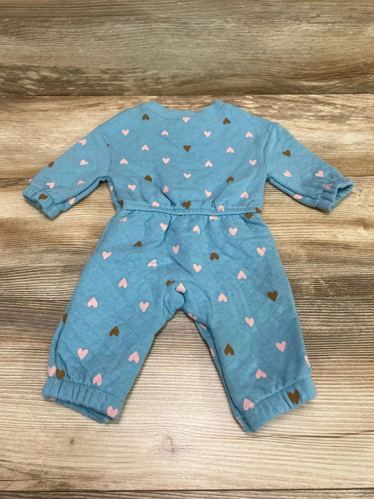 Flat lay of blue quilted baby coverall with pink and brown heart print showing elastic ankle cuffs and gathered waist on wooden background
